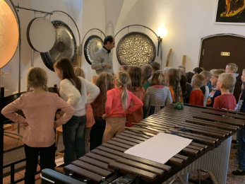 Gruppe Kinder stehend vor verschiedenen Klanginstrumenten und einem Mitarbeiter des Klanggewölbes